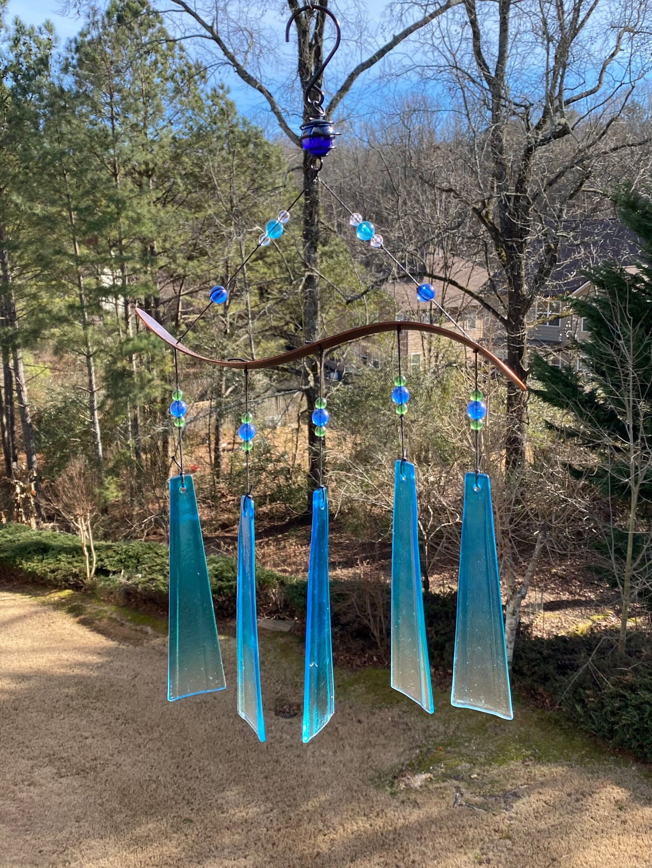 Blue glass wind chimes with crystal accents hanging from tree branches in a garden