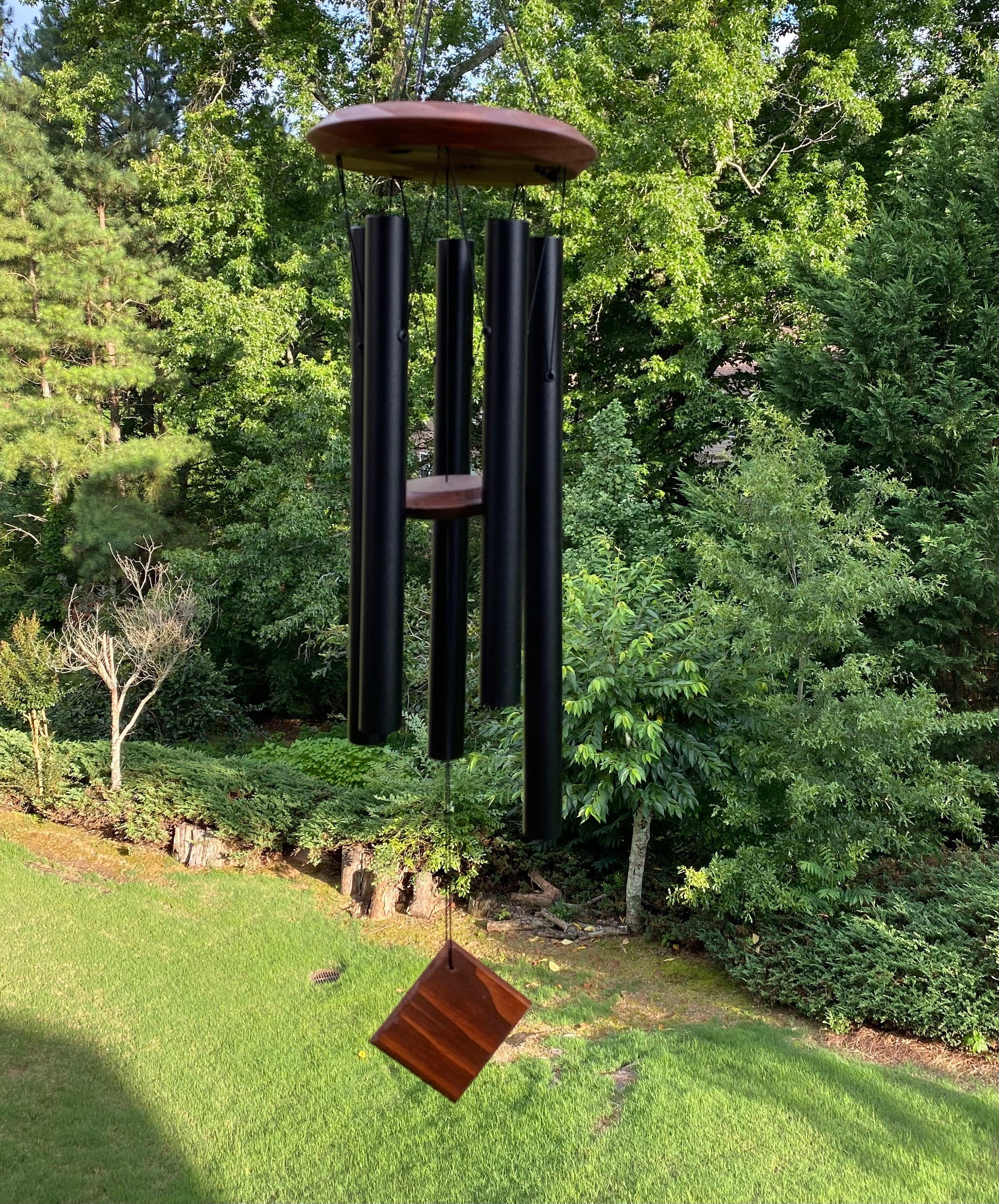 Wind chime with black tubes and wood accents hanging outdoors for peaceful ambiance