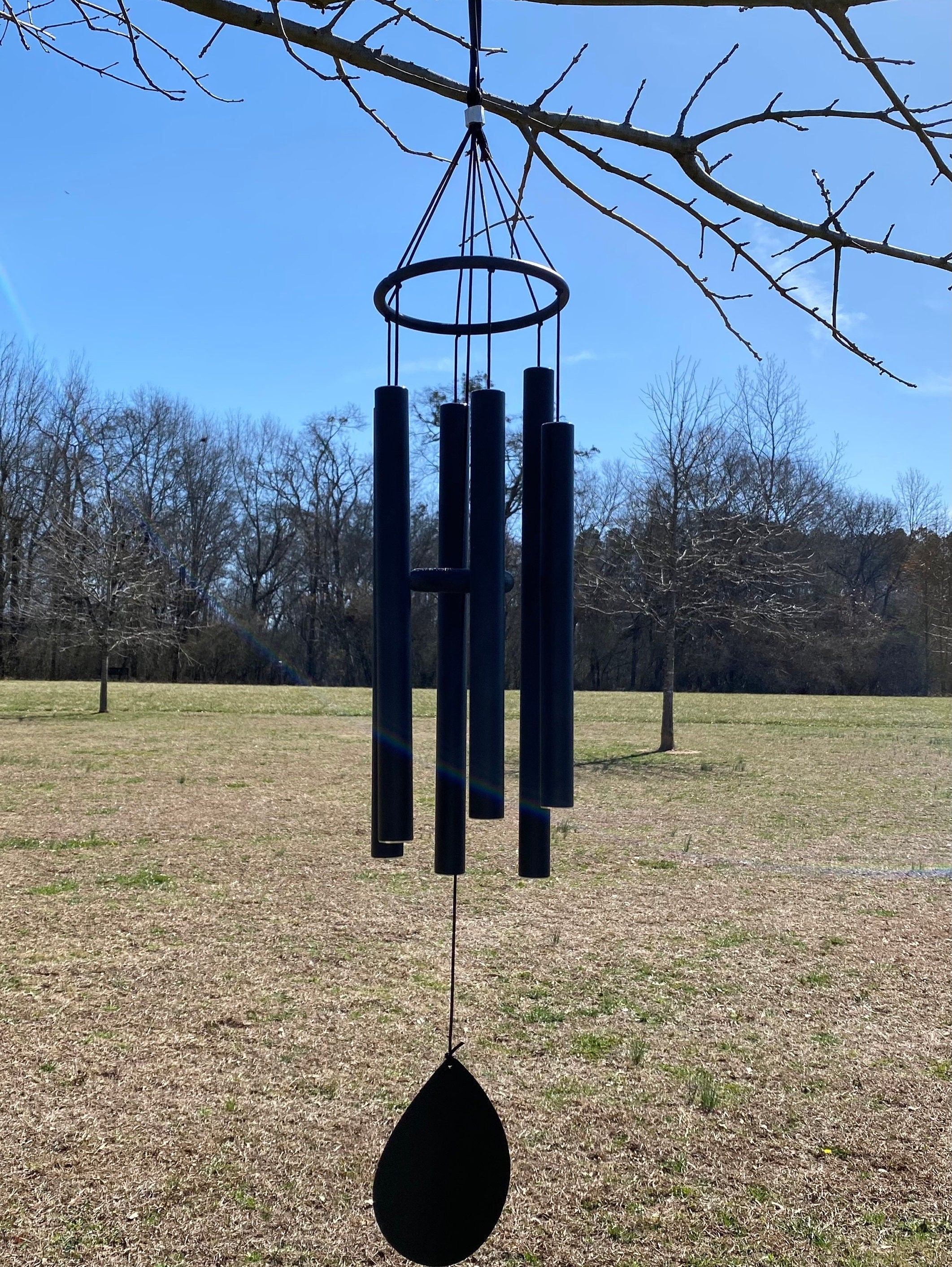 Black metal wind chimes hanging from a tree branch for peaceful outdoor ambiance