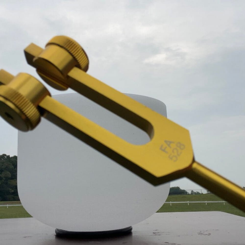 Gold-colored 528 Hz Crystal-End Tuning Fork on a white spherical object for healing