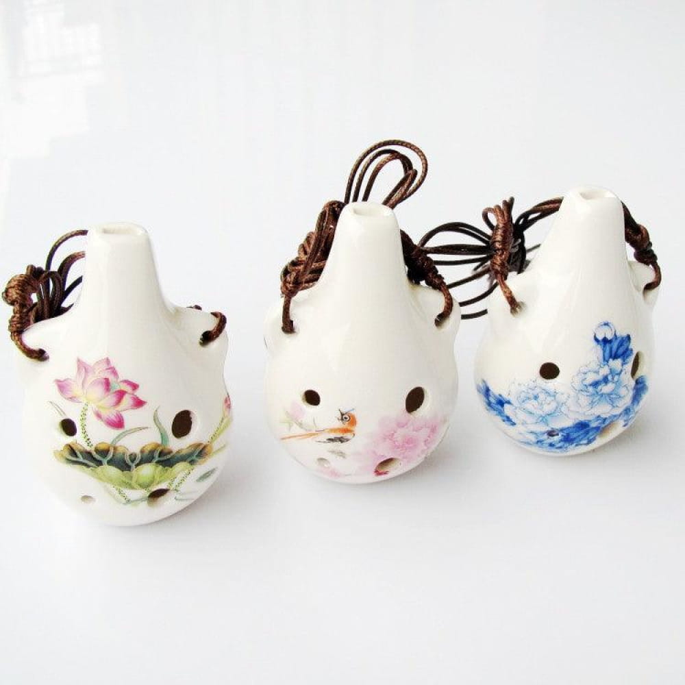 Three white ceramic ocarinas with floral patterns and dark strings for a unique gift