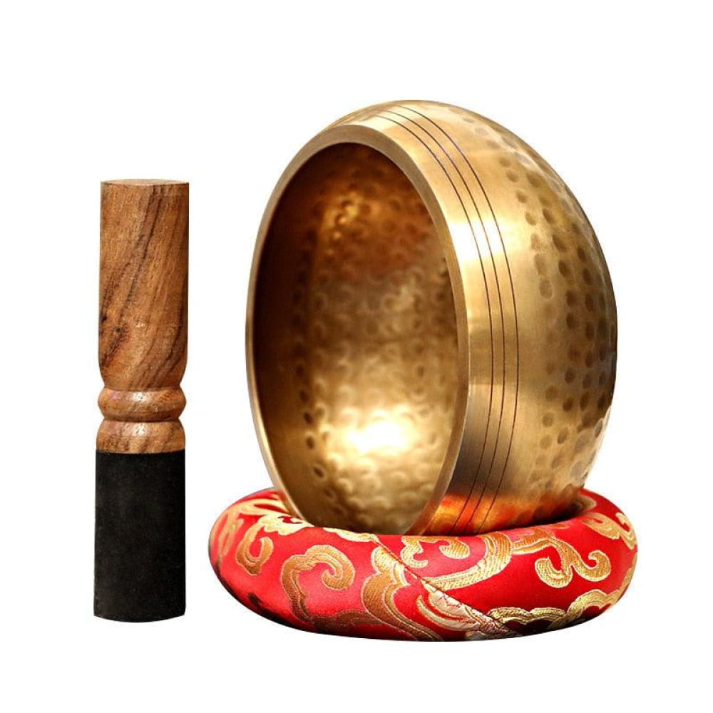 Hammered brass Tibetan singing bowl on red and gold cushion with wooden striker
