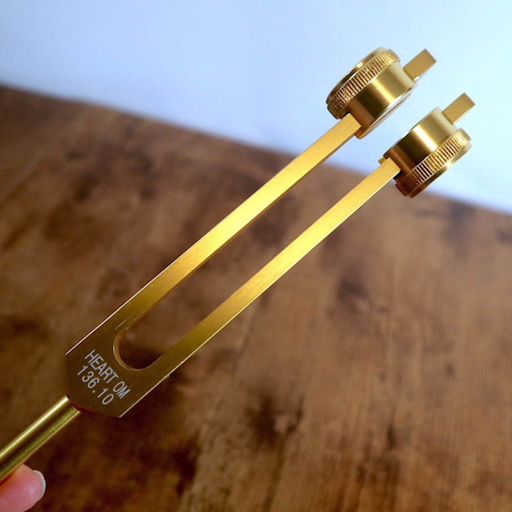 Golden metal tuning fork with adjustable prongs in 136.10 Hz weighted design