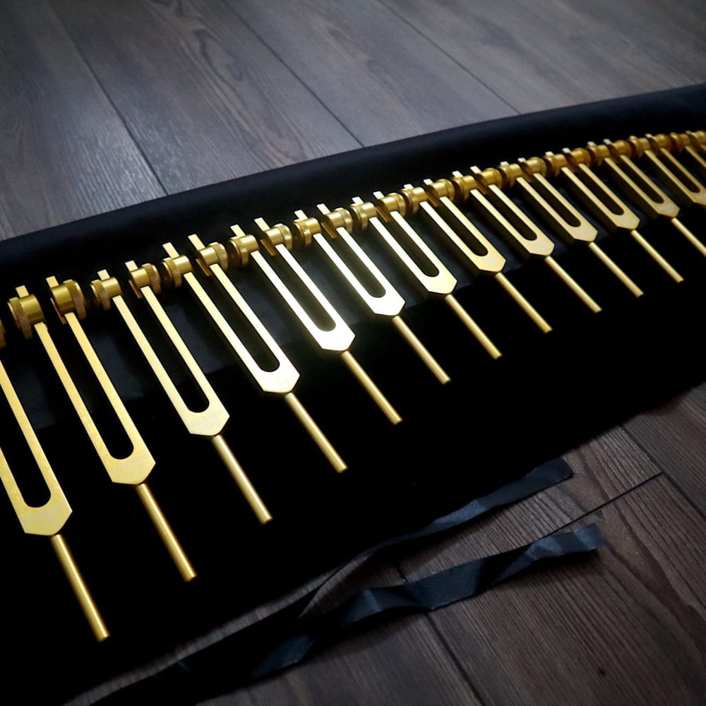 Row of golden tuning forks on black surface for healing in 15pc Tuning Fork Set