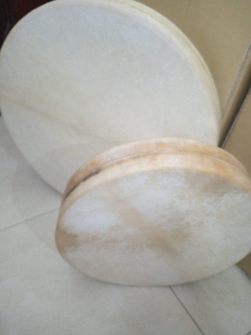 White round pillow with beige accents next to 16’’ Ocean Drum Instrument with wave beads