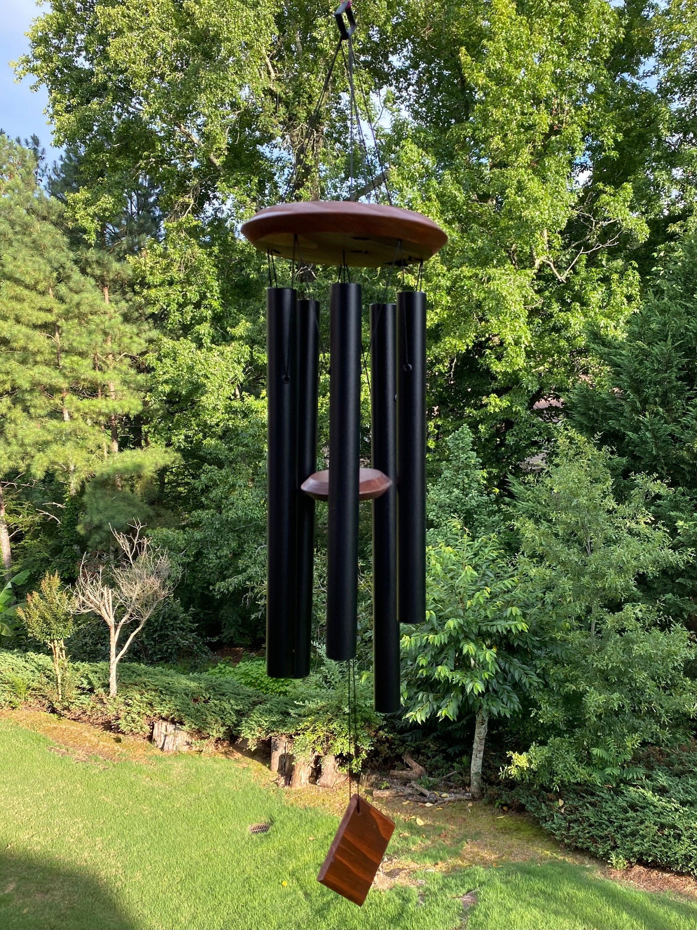 Black metal wind chime with wooden top swaying gently in the breeze for outdoor decor