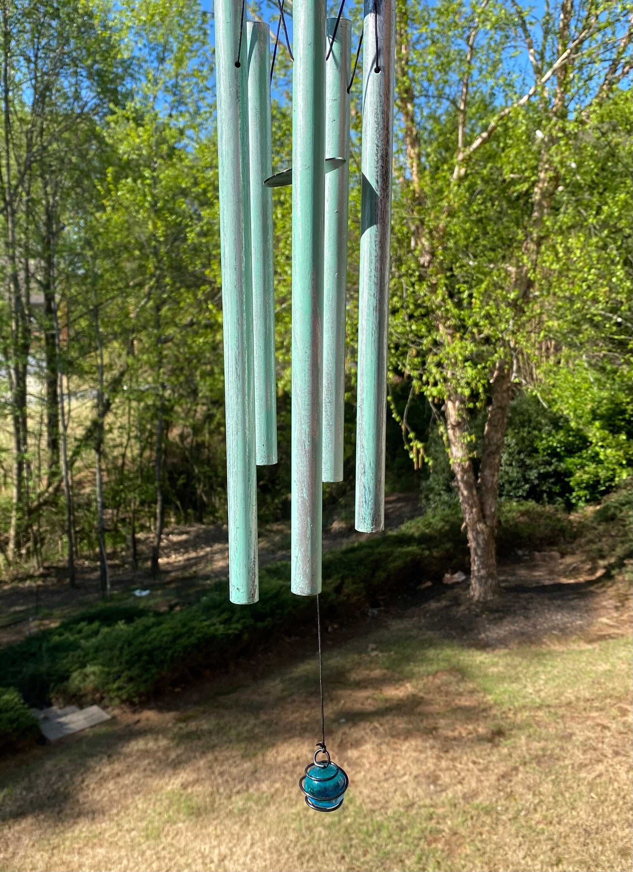 Turquoise wind chimes with vertical metal tubes in an outdoor setting