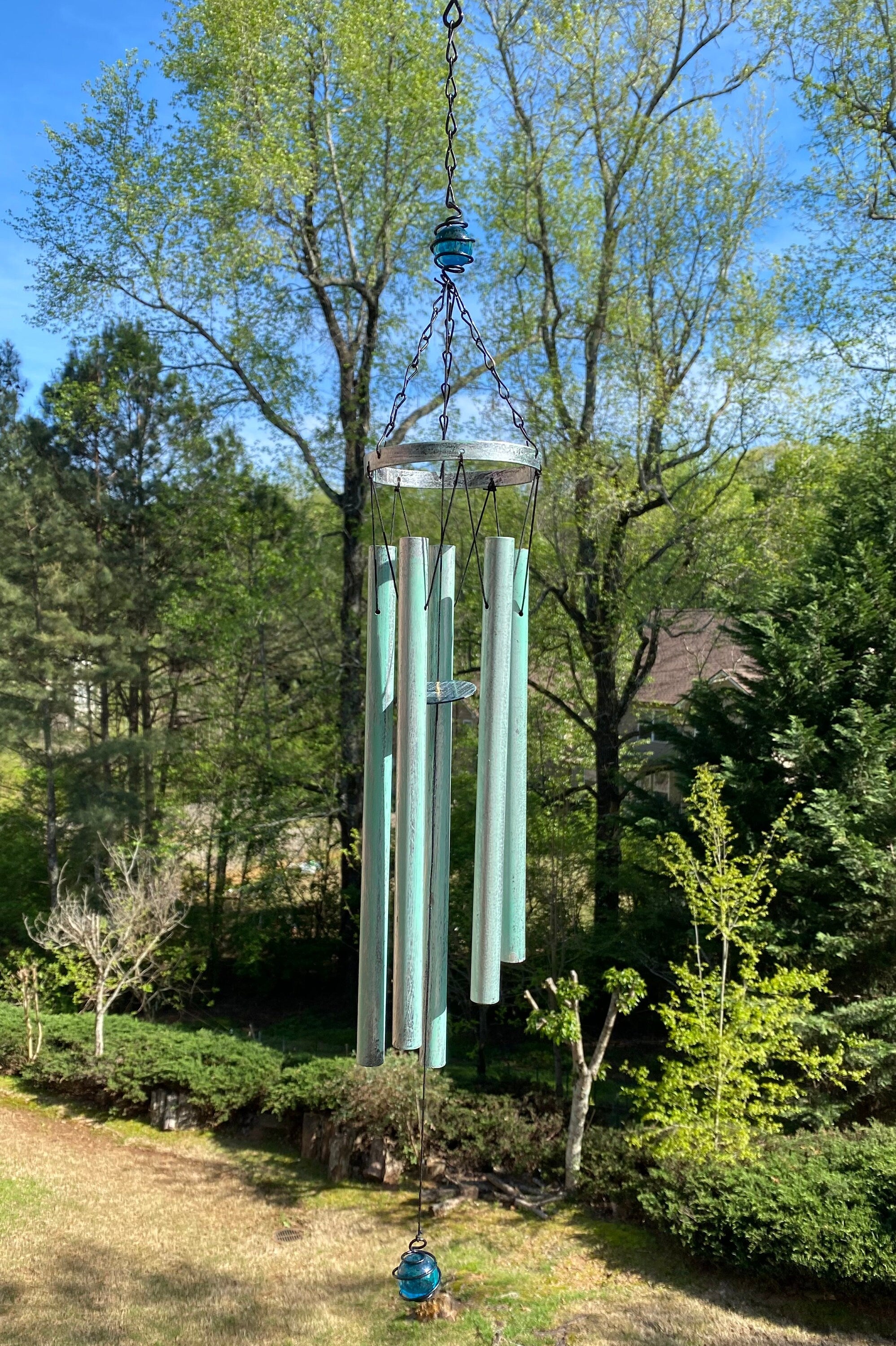 Turquoise wind chimes hanging from a tree branch in a serene outdoor setting