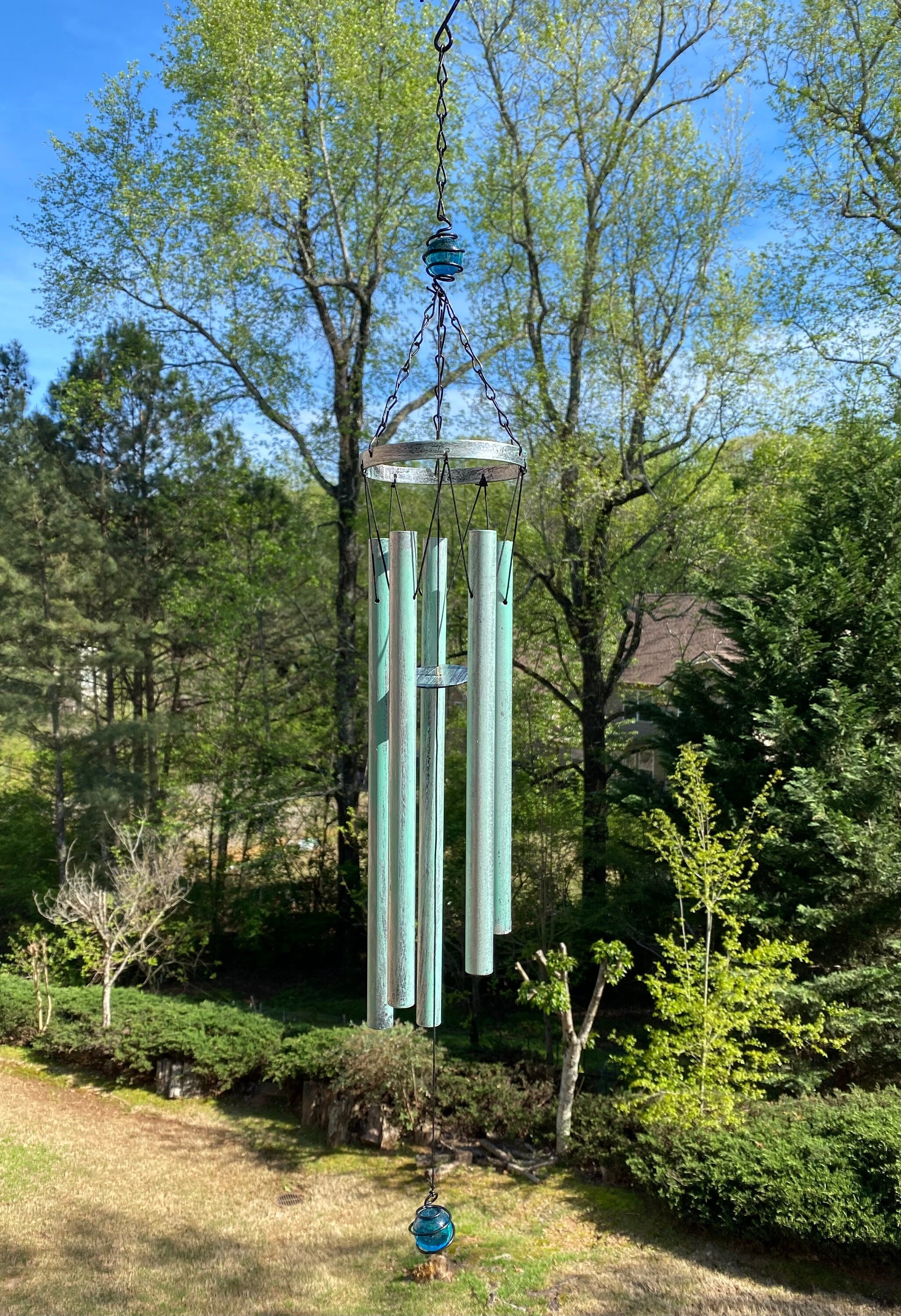 Turquoise wind chimes hanging from a tree branch, featuring a deep tone metal design