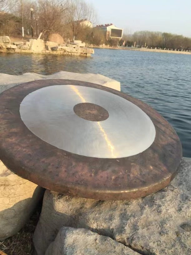 Metallic gong on stone pedestal near water for meditation and sound healing