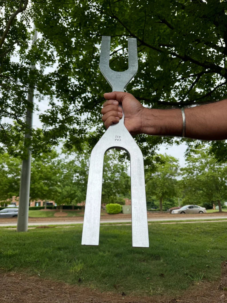 White tuning fork metal sculpture held by hand for 432 Hz and 528 Hz dual frequency healing