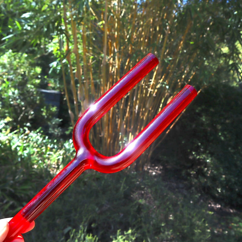 Red plastic devil’s pitchfork toy next to 528Hz Crystal Giant Tuning Fork for sound healing