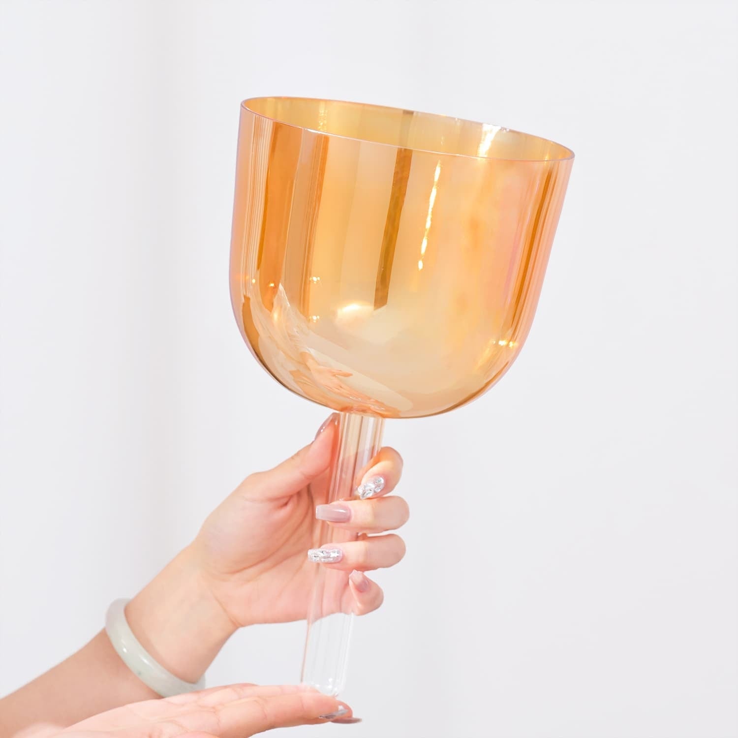 Peach-colored glass wine goblet held by a hand next to 6’’ F Note Crystal Singing Bowl