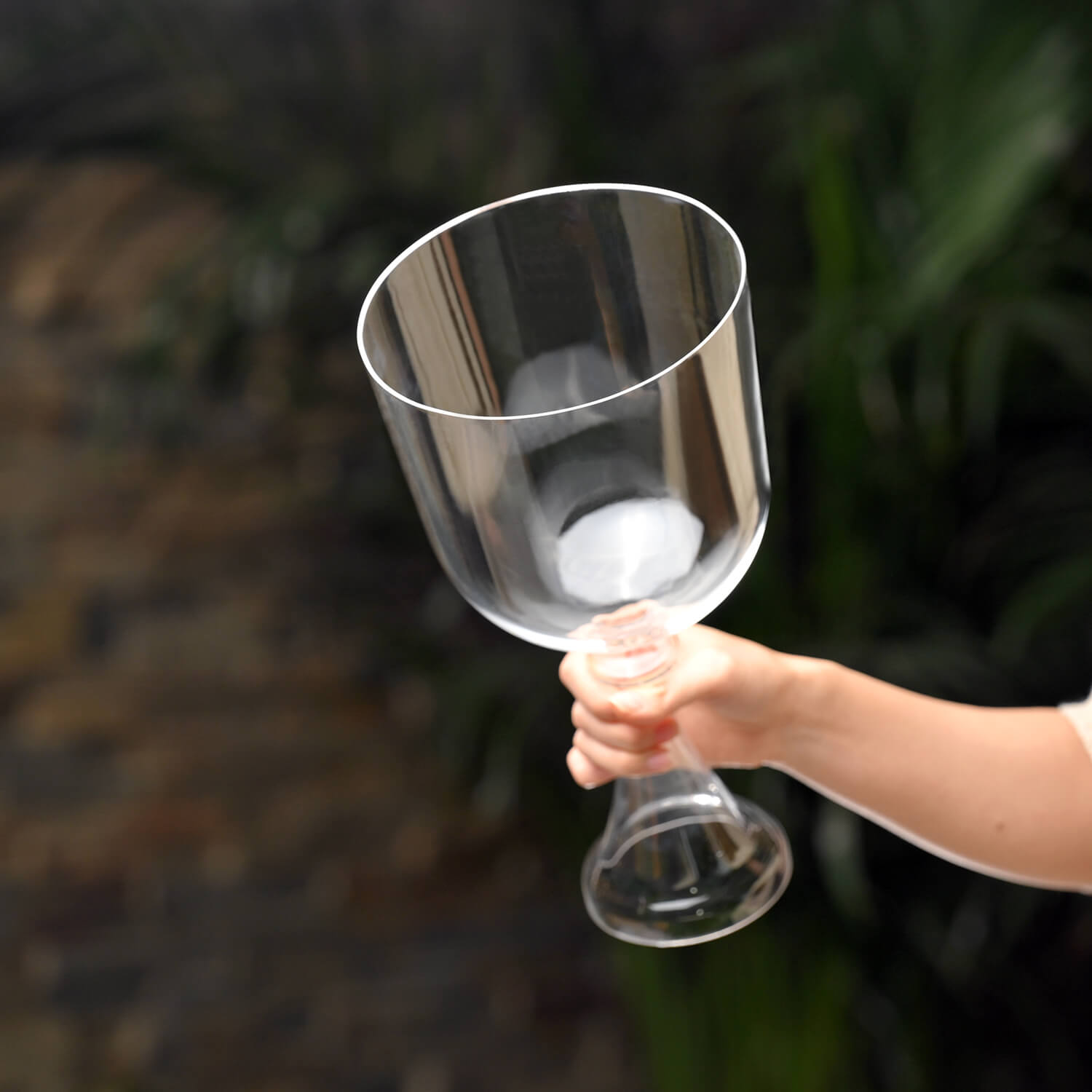 Clear wine glass held by hand next to 6 inch Quartz Crystal Singing Bowl with Handle