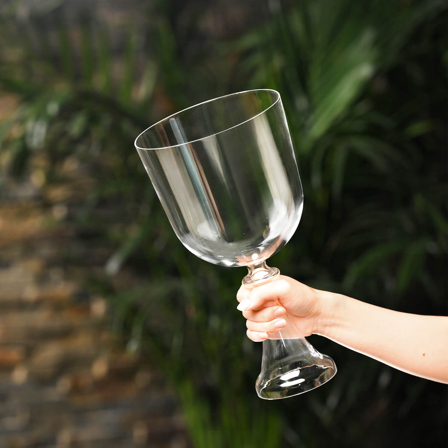 Hand holding a tilted clear glass wine goblet next to a Quartz Crystal Singing Bowl