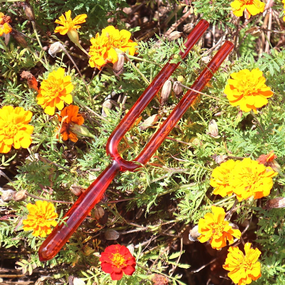 Red glass tuning fork among marigold flowers in 8pc Crystal Tuning Fork Set