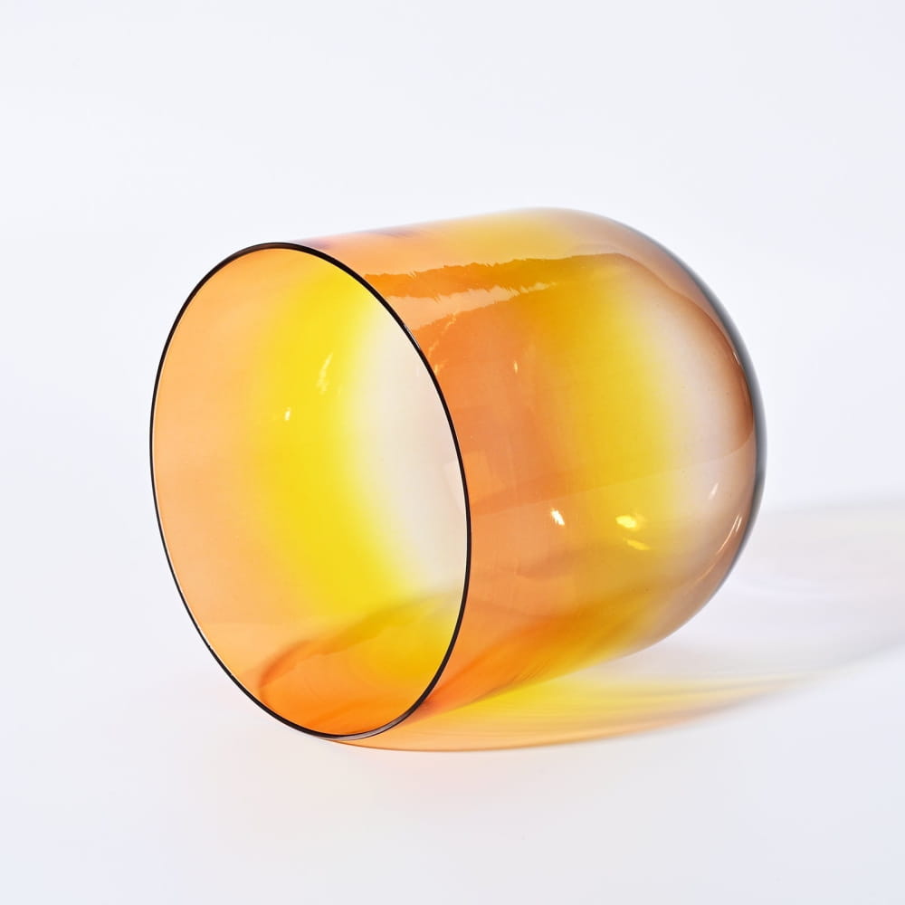 Amber-colored glass tumbler lying on its side beside Alchemy Clear Rainbow D Note Crystal Singing Bowl