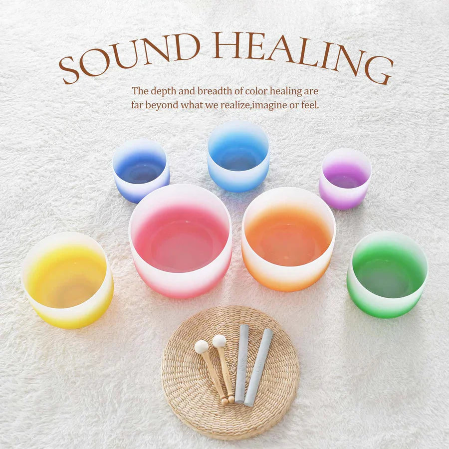 Crystal singing bowls in vibrant colors with tuning forks on a woven mat