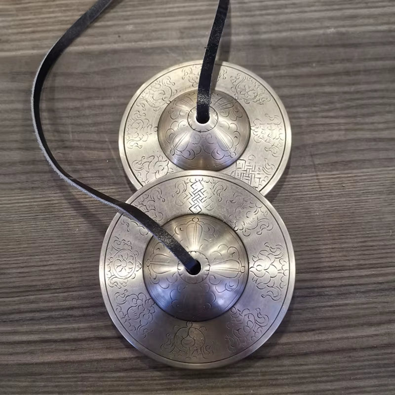 Brass Buddha Hand Cymbals with intricate designs connected by black cord for meditation