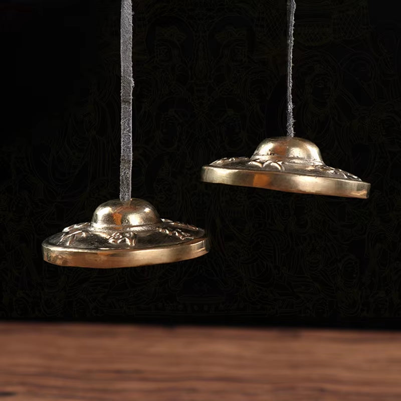 Two ornate metal serving domes suspended by cords for Brass Tingsha Buddha Hand Cymbals