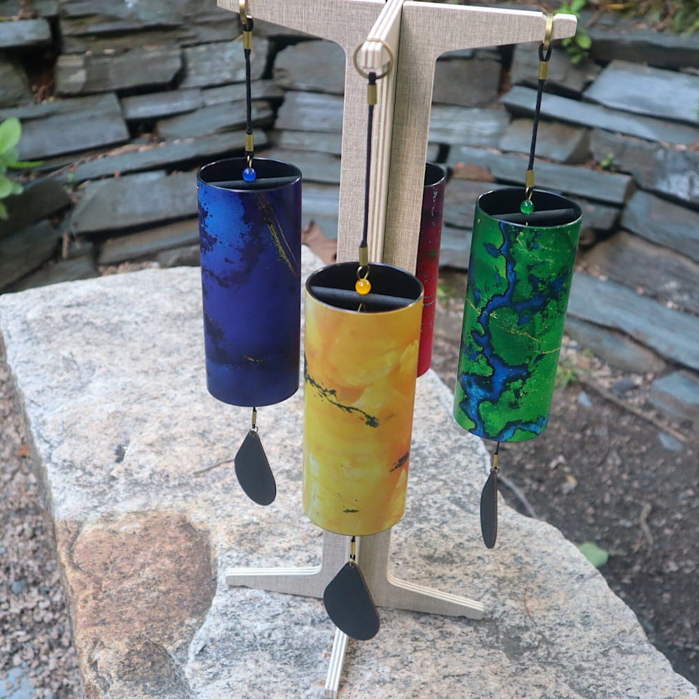 Three colorful Koshi wind chimes hanging from a wooden stand in a set of four elements