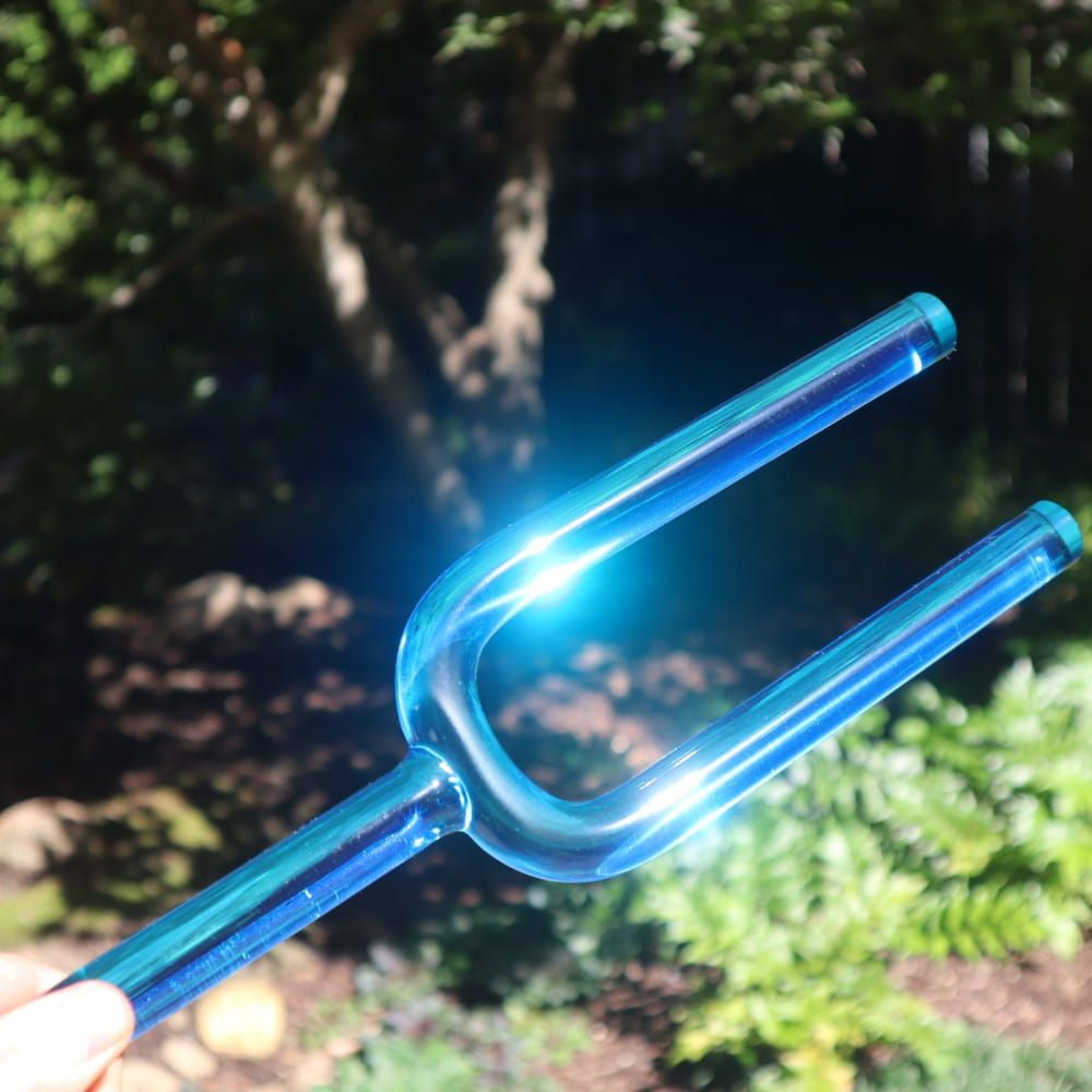 Bright blue glass tuning fork glowing in sunlight from Crystal Tuning Fork Set