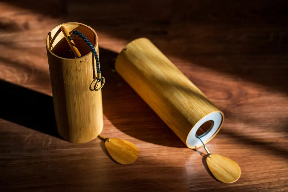 A natural bamboo wind chime with a warm golden hue, featuring two hanging wooden discs and a cylindrical body that holds the striker.