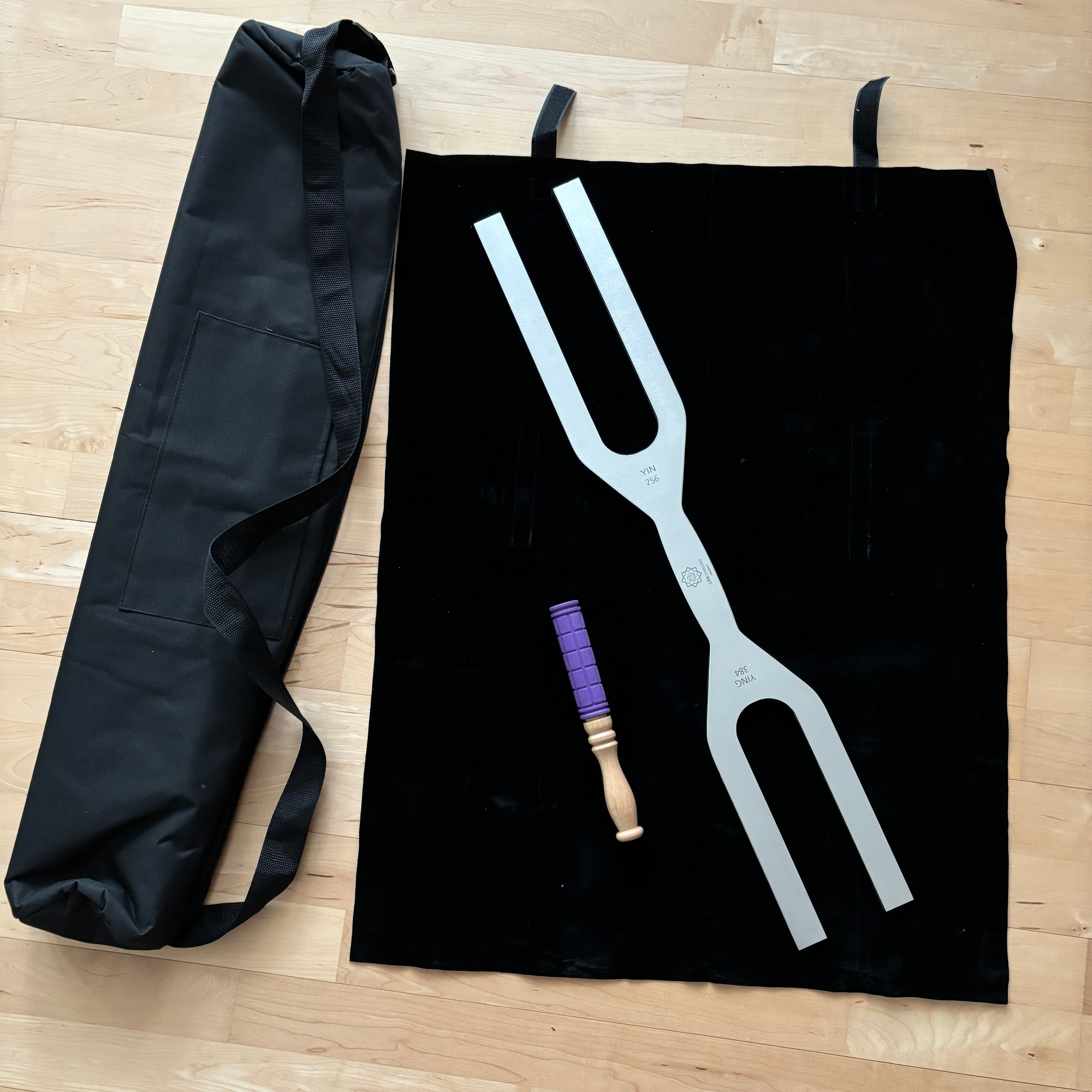 Giant Tuning Fork with purple handle on black fabric beside carrying case