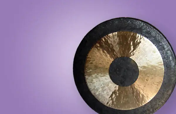 A circular gong with a polished golden center and dark, textured outer rim.