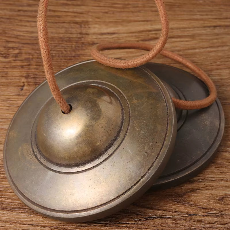 Pair of metallic Tibetan meditation cymbals with brown cord for yoga and mindfulness