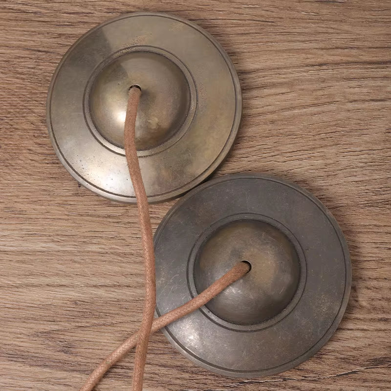 Pair of metallic finger cymbals with leather cords for meditation and yoga