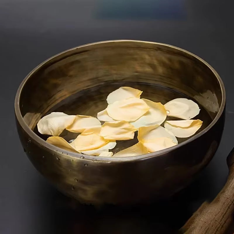 Dark ceramic bowl with floating rose petals, enhancing Handmade Copper Tibetan Singing Bowl