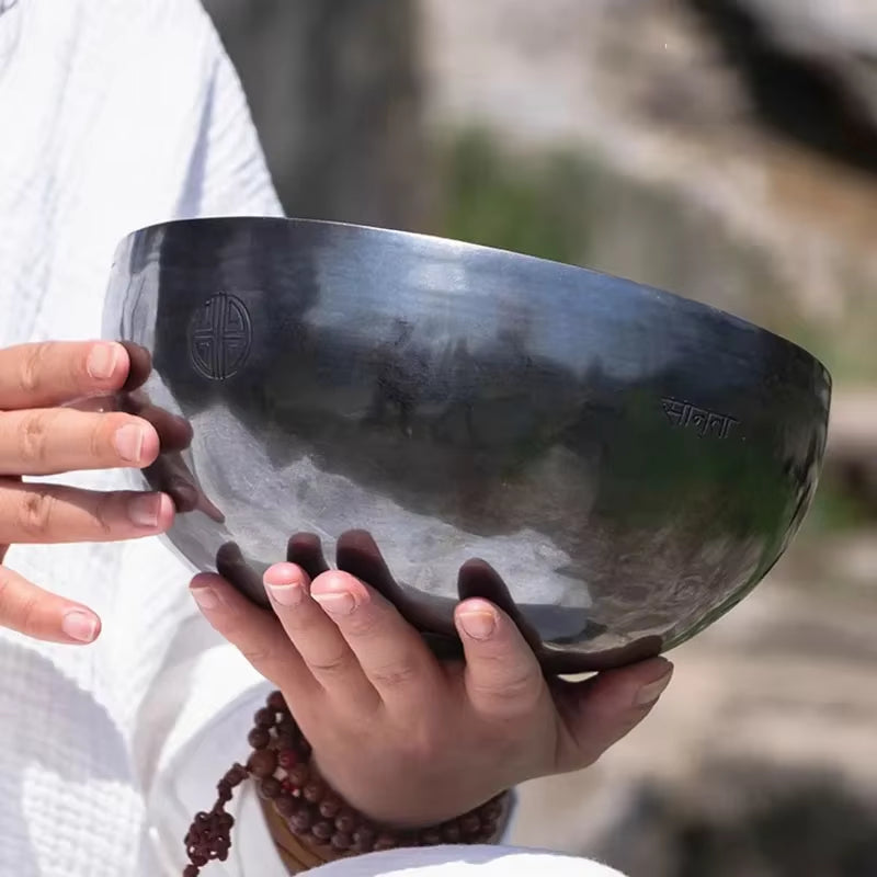 Dark metallic Tibetan singing bowl held by hands with prayer beads for meditation