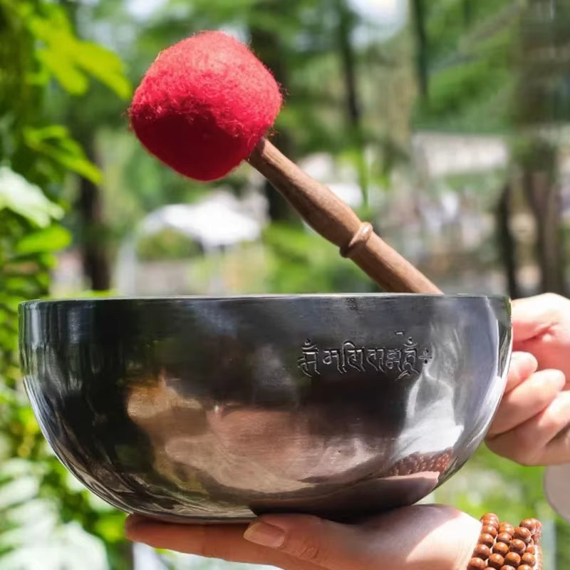 Dark metallic Tibetan singing bowl with red-tipped wooden mallet for meditation healing