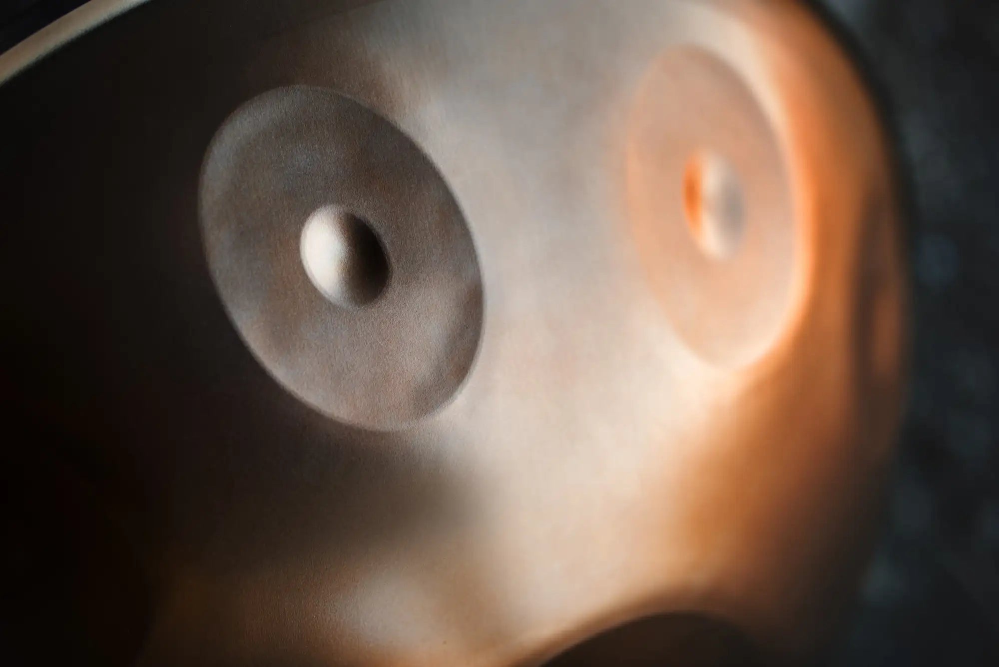A metallic, circular object with two distinct eye-like features—one dark and one glowing orange—suggesting a futuristic or robotic design.