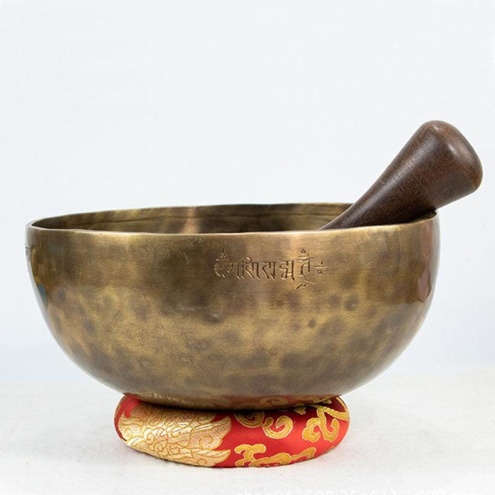 Hammered brass Tibetan singing bowl with wooden striker on red decorative cushion