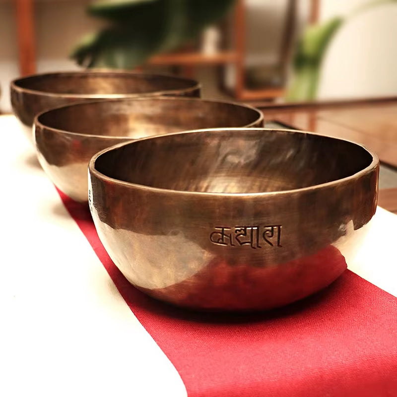 Three metallic Tibetan singing bowls on a red surface for meditation therapy