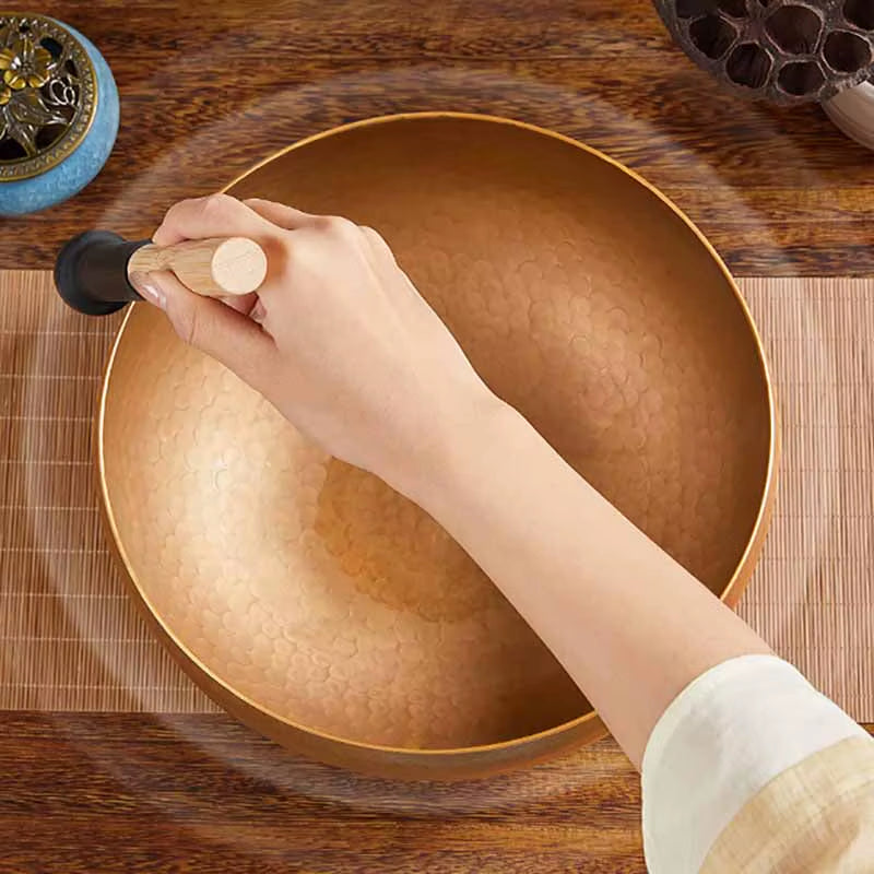 Hand holding a mallet above a large golden Tibetan singing bowl for sound therapy