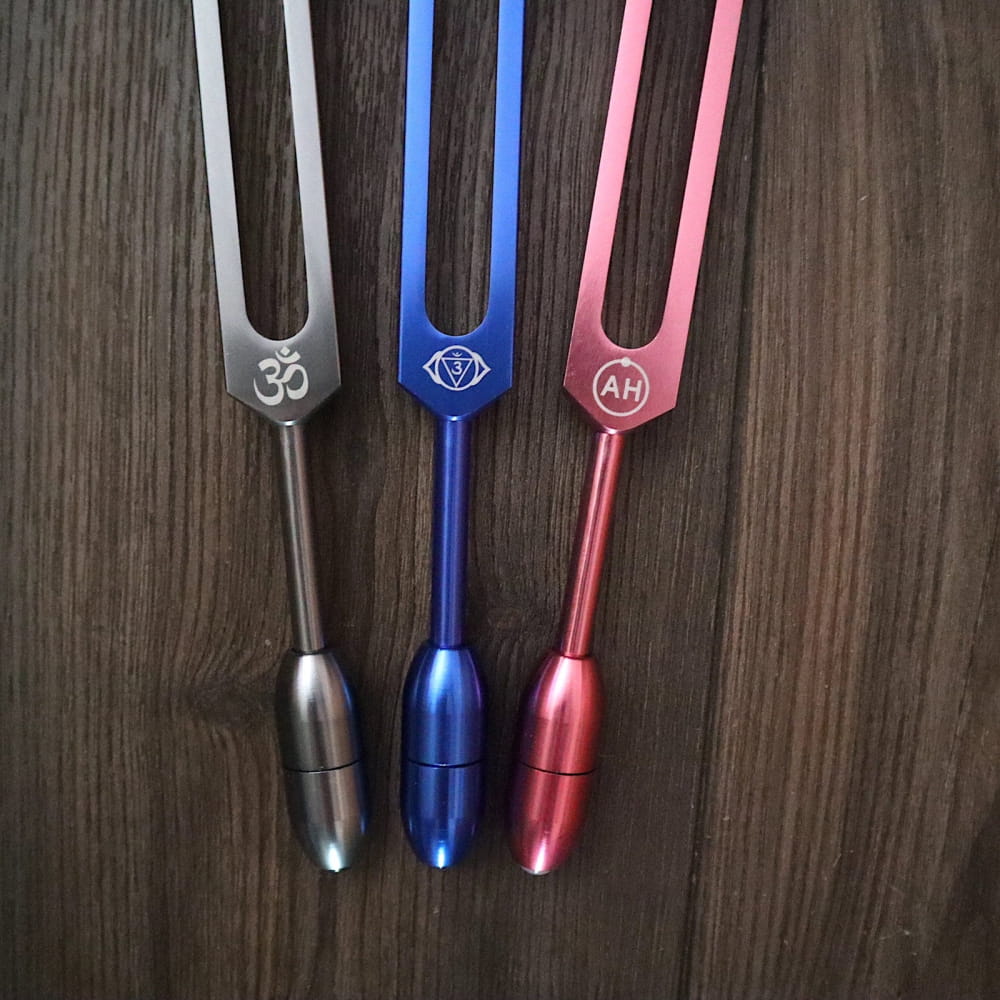 Three tuning forks in silver, blue, and pink with spiritual symbols in a massage set