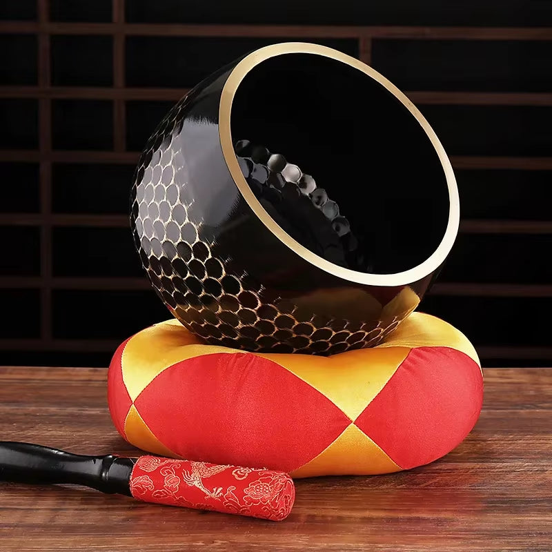 Black ceramic singing bowl with honeycomb pattern and gold rim on cushion for meditation