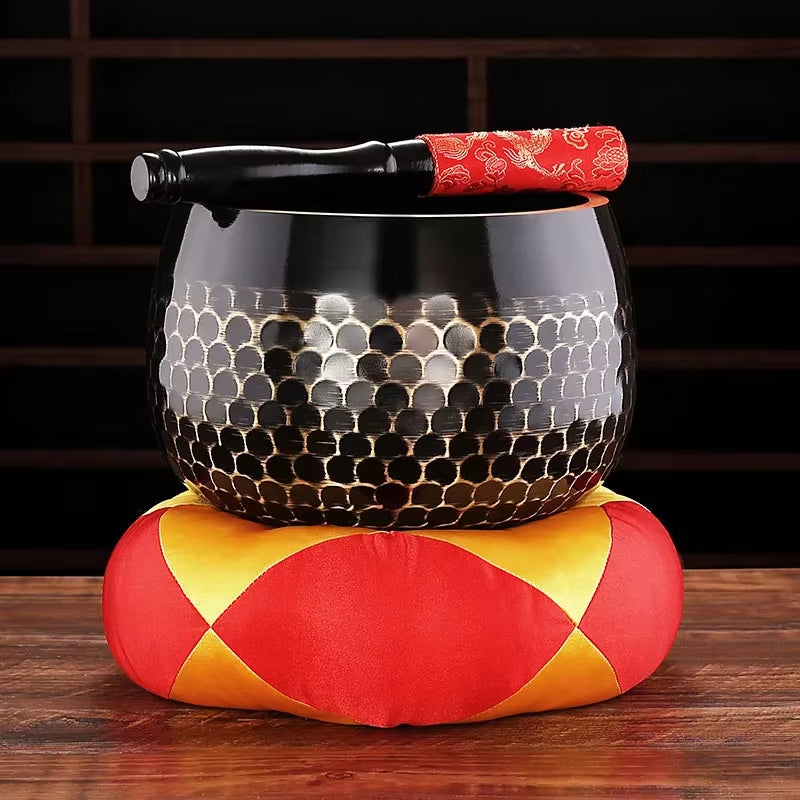 Black ceramic singing bowl with honeycomb pattern on red and yellow cushion for meditation