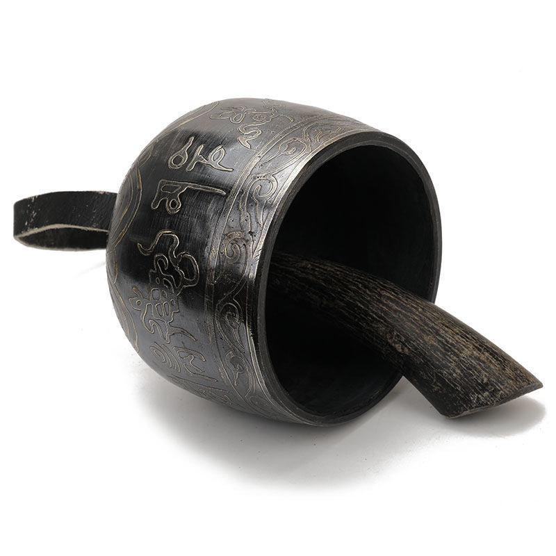 Black ceramic mug with ornate engravings beside Tibetan Meditation Bell for relaxation