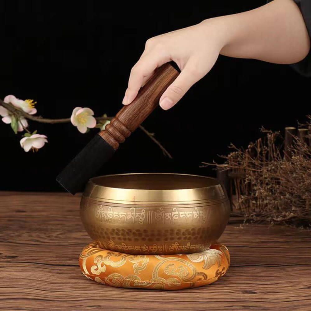 Brass Tibetan singing bowl on ornate cushion with wooden striker for meditation