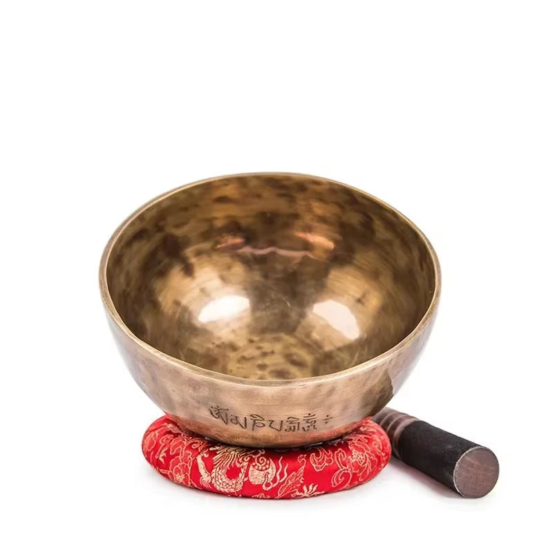 Hammered brass Tibetan Singing Bowl on a red cushion with a striker for meditation