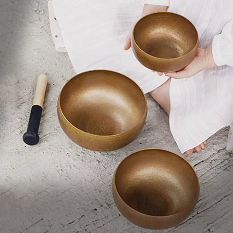 Three golden Tibetan singing bowls with a striker for meditation and healing