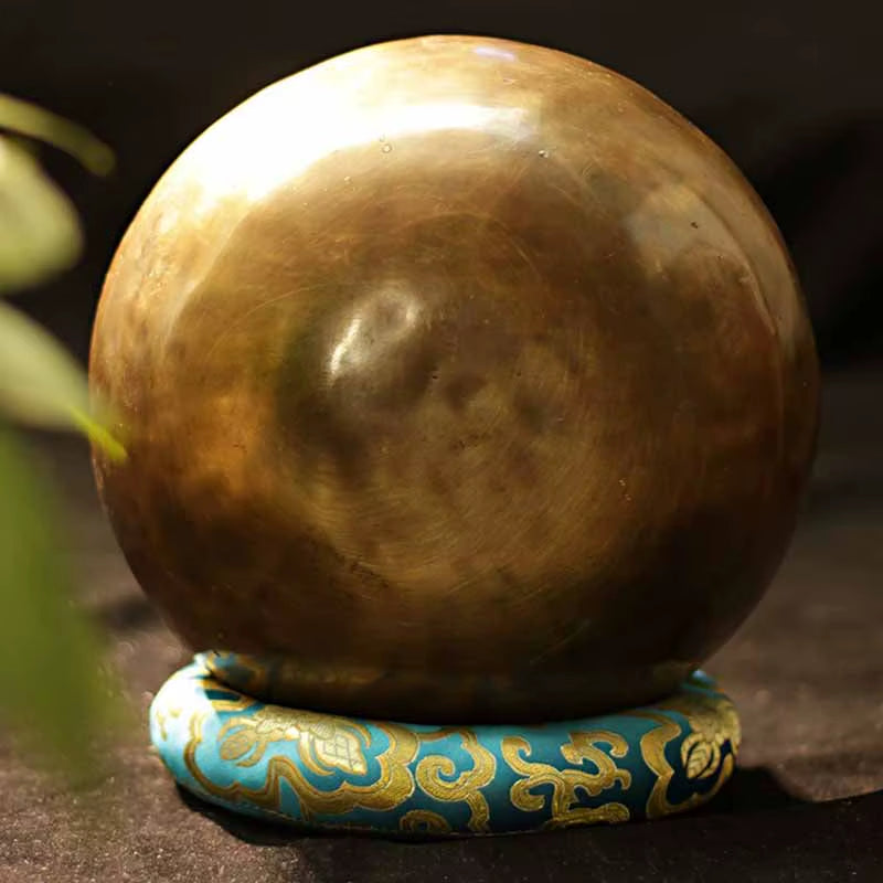 Metallic bronze sphere on turquoise and gold cushion with Tibetan Singing Bowl