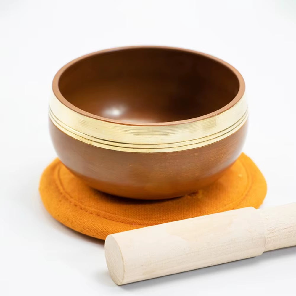 Brown ceramic Tibetan singing bowl set on orange cushion with white striker