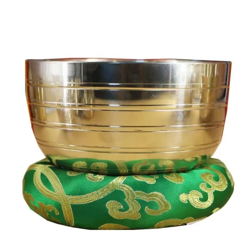 Metal Tibetan Singing Bowl on green cushion with gold Om symbols for sound healing