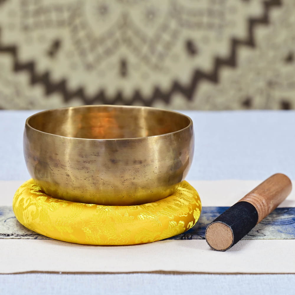 Brass Tibetan Sound Bowl on yellow cushion with wooden striker for meditation healing