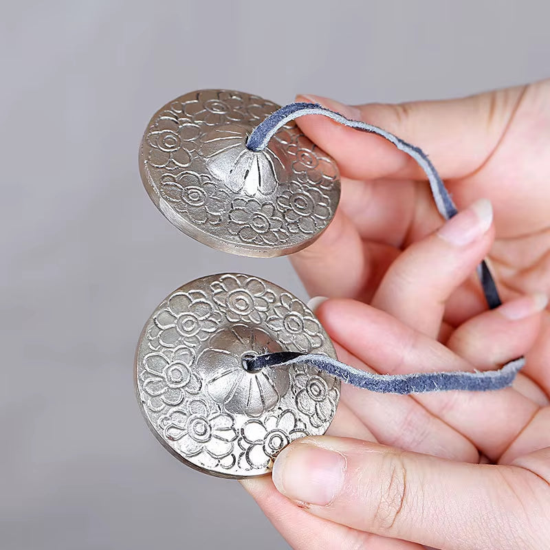 Pair of decorative silver Tibetan Tingsha hand cymbals connected by blue cord